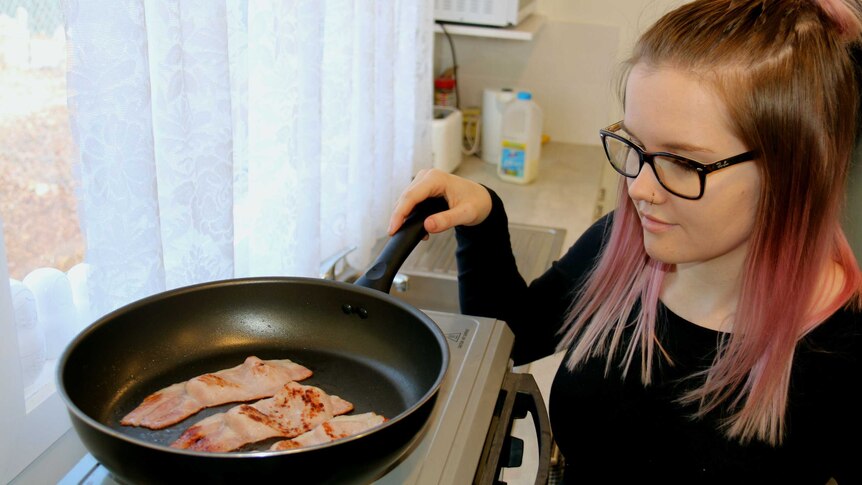 A woman cooks bacon on a stove top.