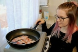 A woman cooks bacon on a stove top.