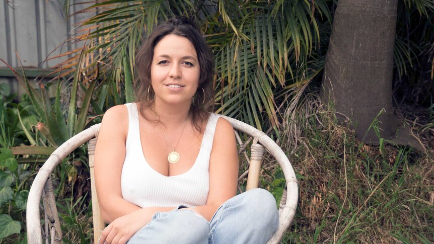 Steph Tsimbourlas smiles while sitting in a leafy garden.