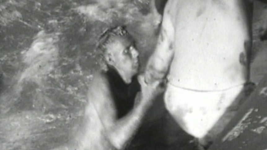 A black-and-white image of a man rescuing another man in the water.