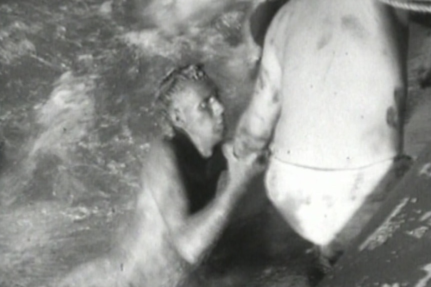 A black-and-white image of a man rescuing another man in the water.