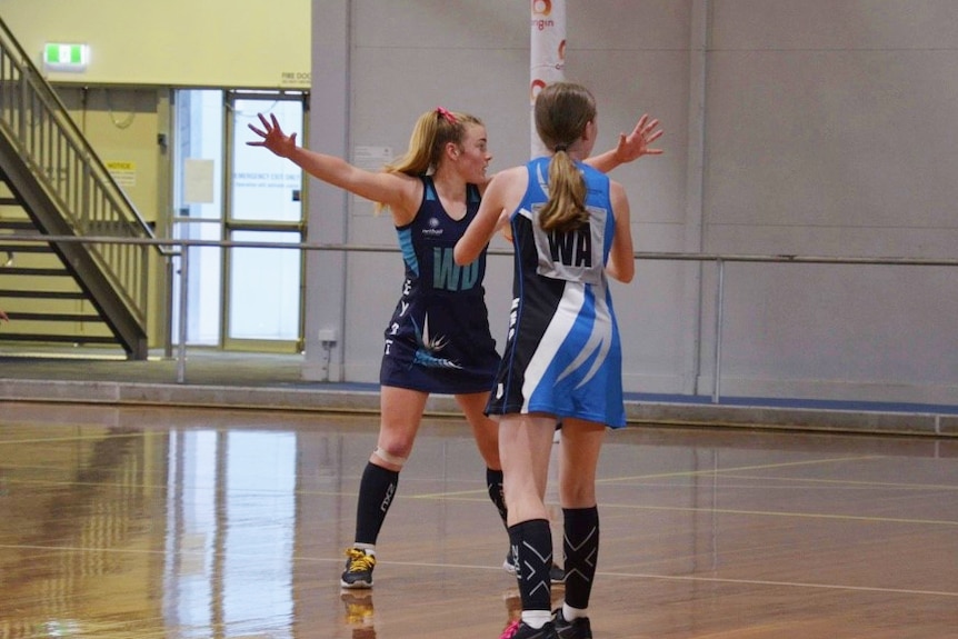a girl blocking another from shooting a goal on a netball court