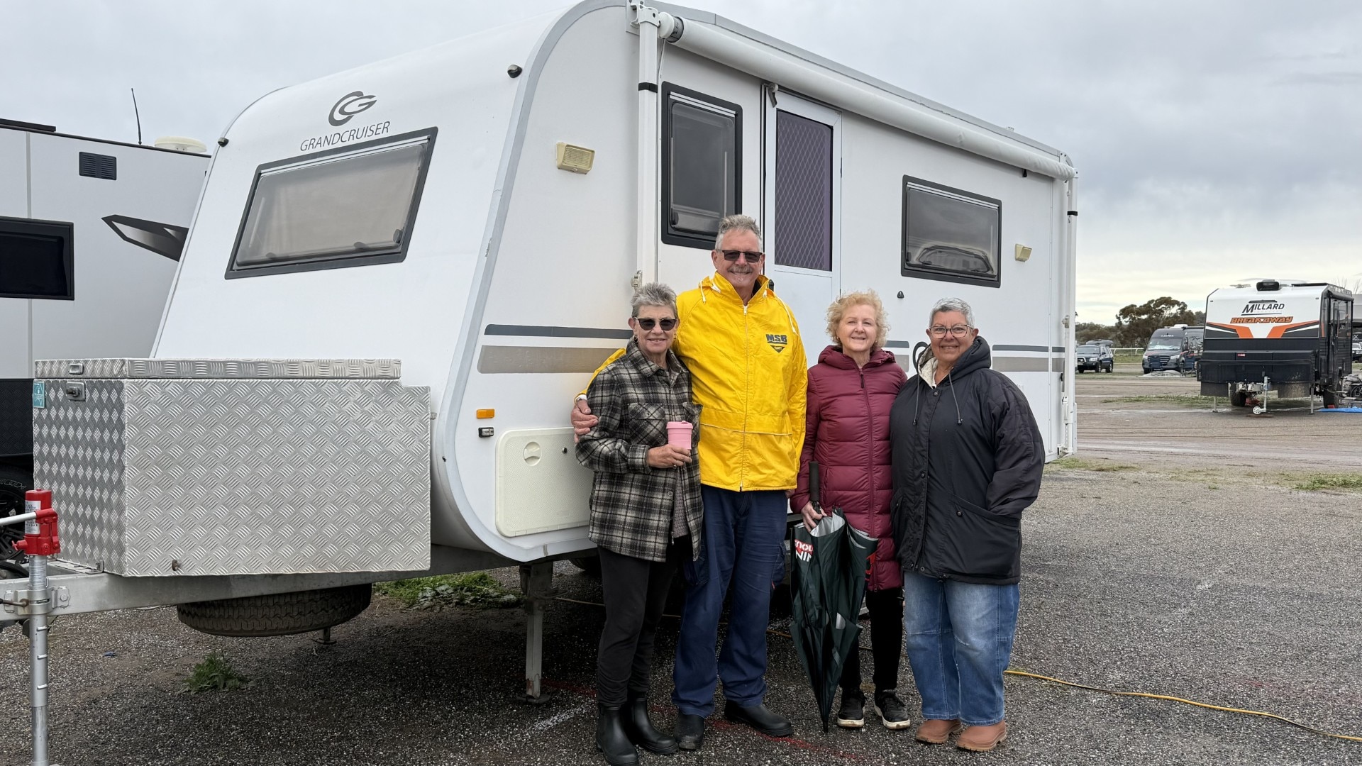 Three women and a man stand in front of a caravan.