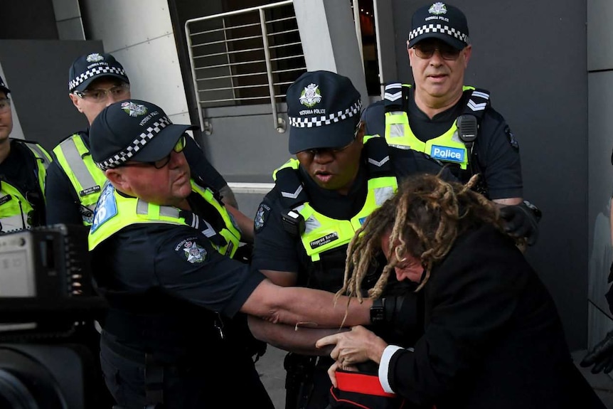 Several police clash with a female demonstrator outside a building.