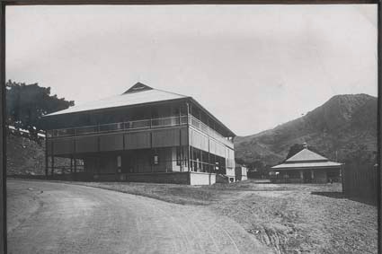 A black-and-white photo of the old hospital with a dirt road and mountain in the background. 