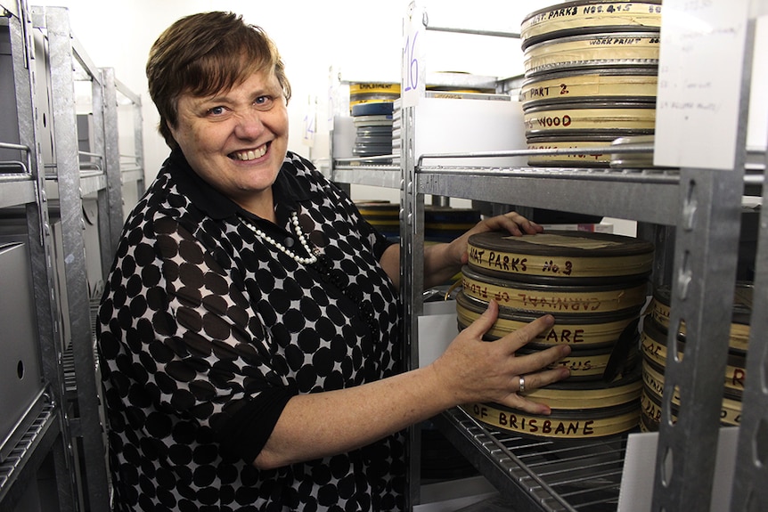 A woman in a black and white shirt stands beside a shelf stacked with film reels.