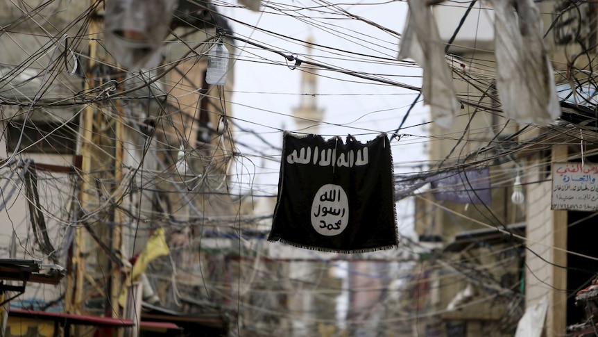 An Islamic State flag hangs amid electric wires over a street.