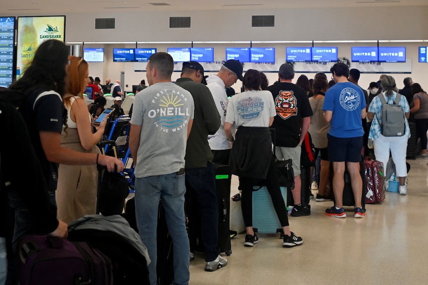 The backs of airport travellers standing in a line at ticket counters inside a Puertor Rican airport.