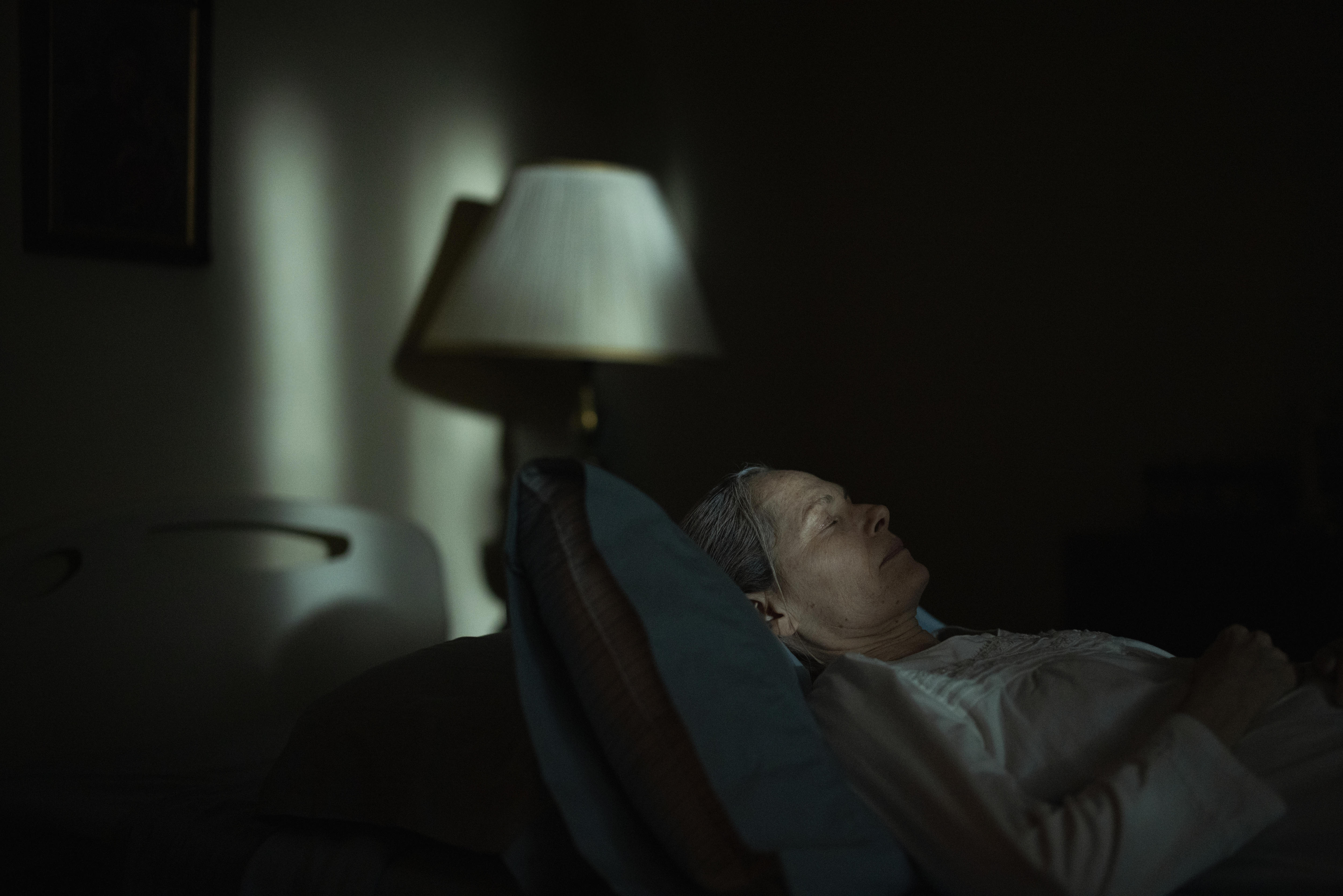 Una anciana yace en una cama en una habitación oscura