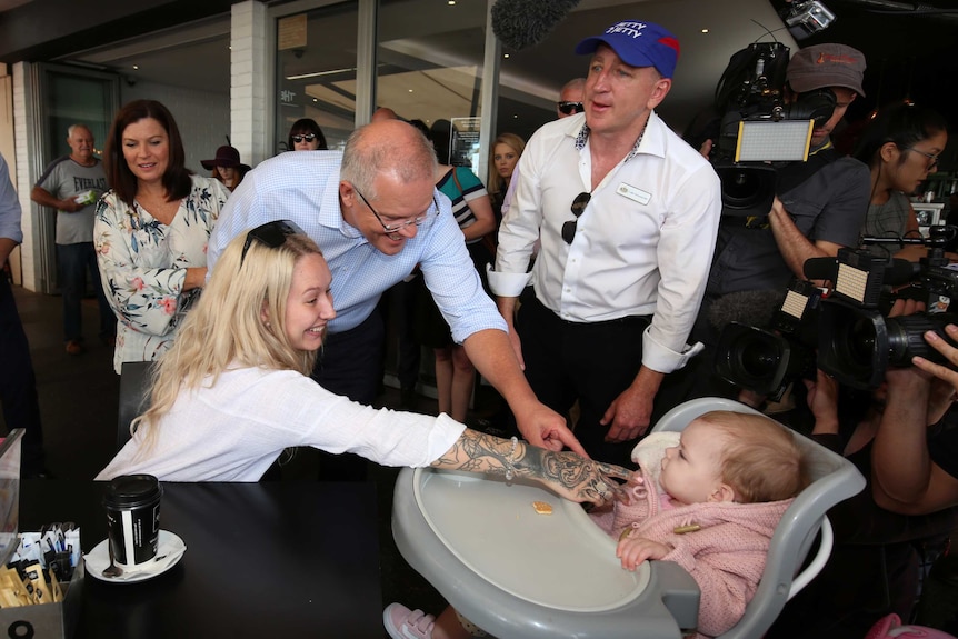 Mr Morrison reaches for a child, whose mother is trying to make her laugh