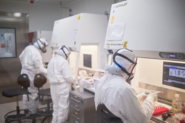 Three scientists wearing full PPE analyse samples in a lab. 