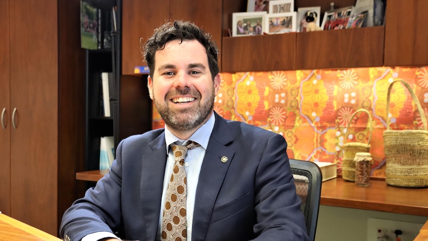 a politican in a suit smiles at the camera while sitting in an office in NT parliament. 