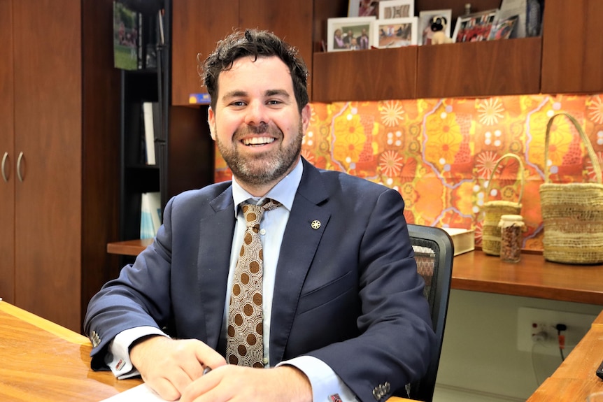 a politican in a suit smiles at the camera while sitting in an office in NT parliament. 