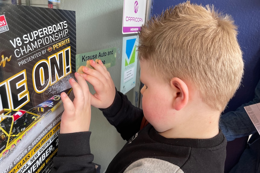 A small boy with blonde hair feels a Braille sticker on a shop front