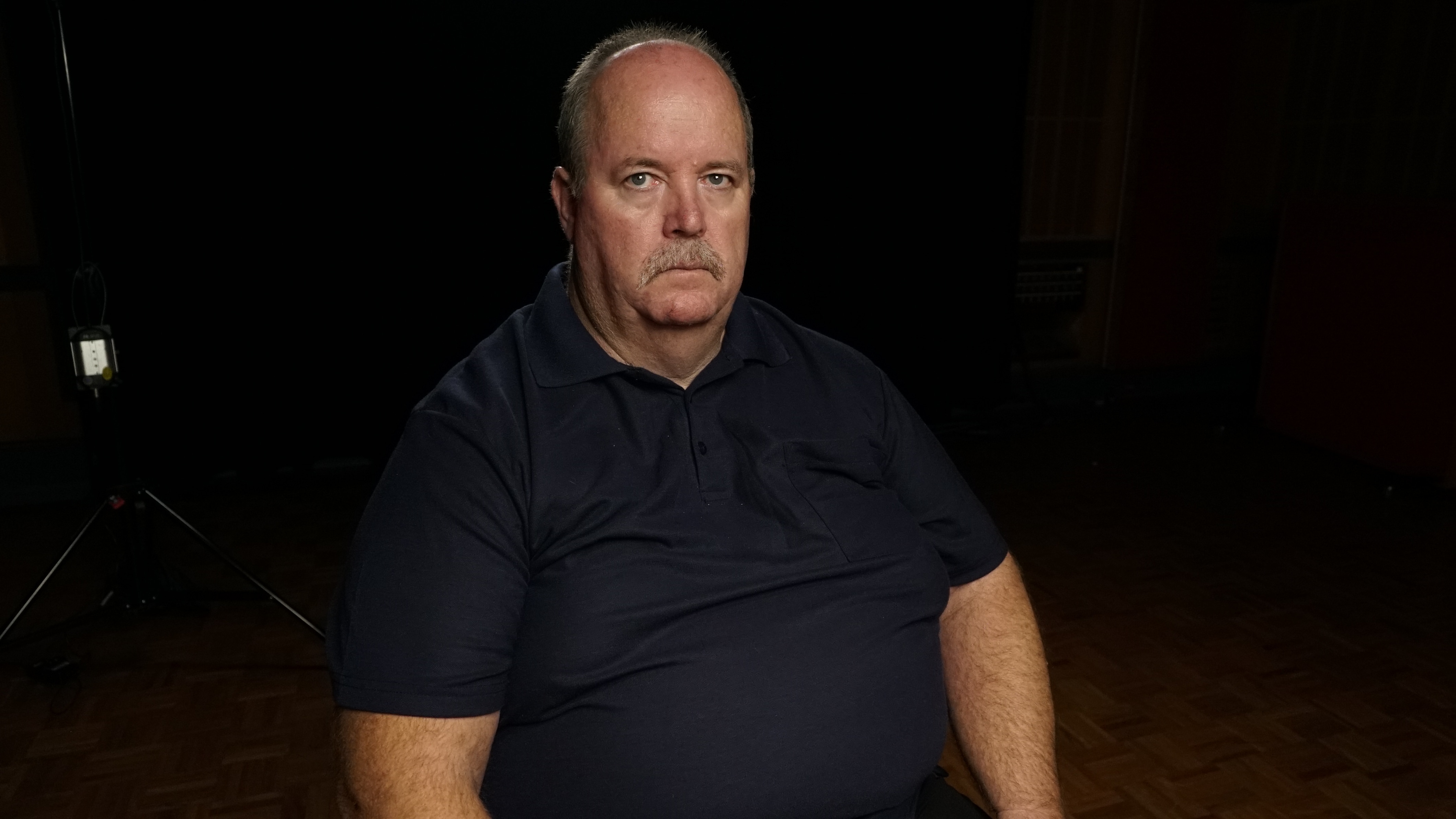 Man sitting in a dark room, wearing a black shirt.