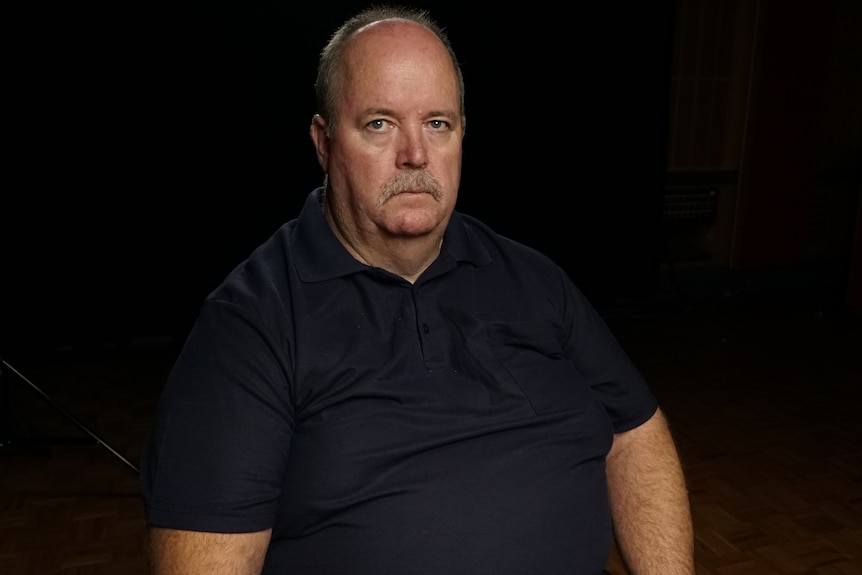 Man sitting in a dark room, wearing a black shirt.