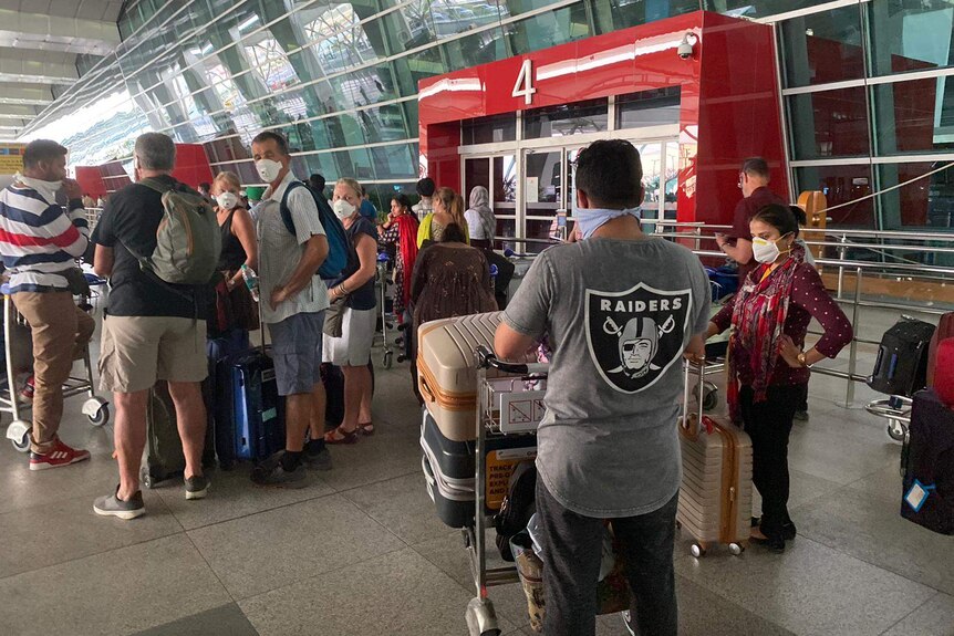 People wearing masks queue at an airport with their luggage.