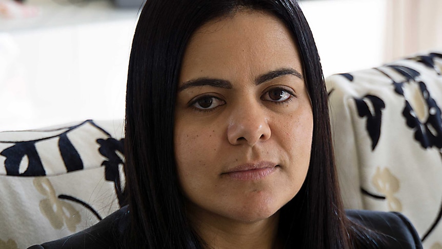 Silvana sits on a couch with a flower pattern. The background is out of focus. She is not smiling.