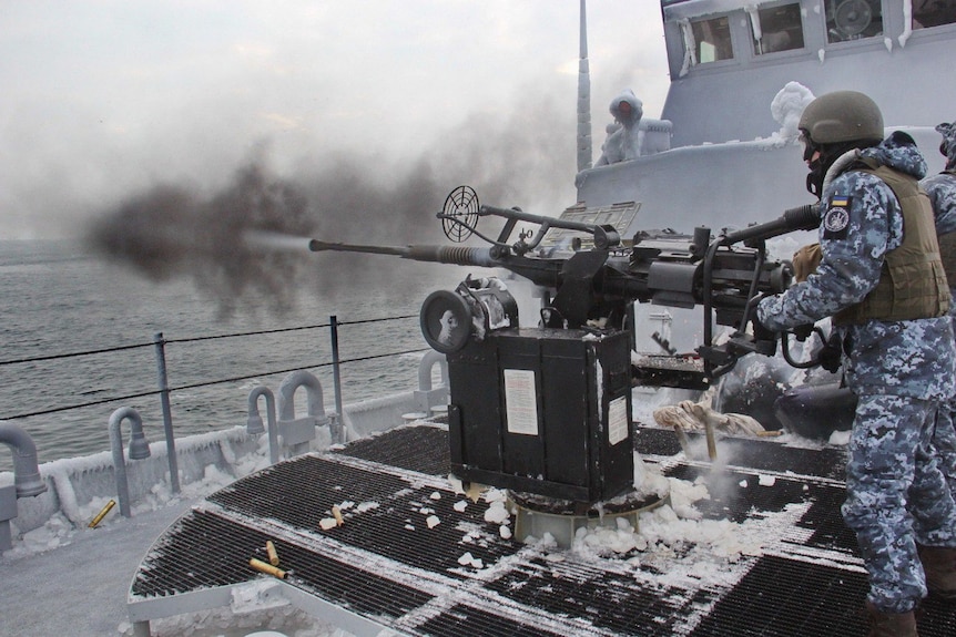 Members of the Ukrainian Navy fire a gun during naval drills on a ship.
