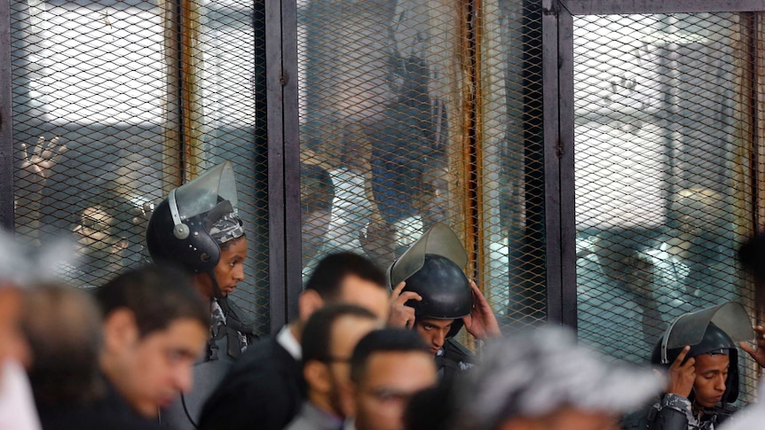 Policemen are seen guarding defendants standing inside a soundproof glass cage at a courtroom.