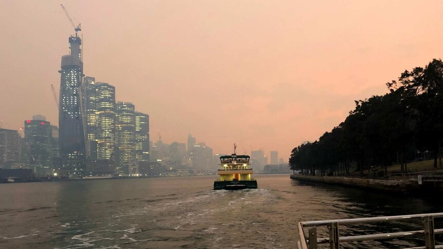 A ferry departs a wharf at Darling Harbour with Barrangaroo shrouded in smoke in the background.