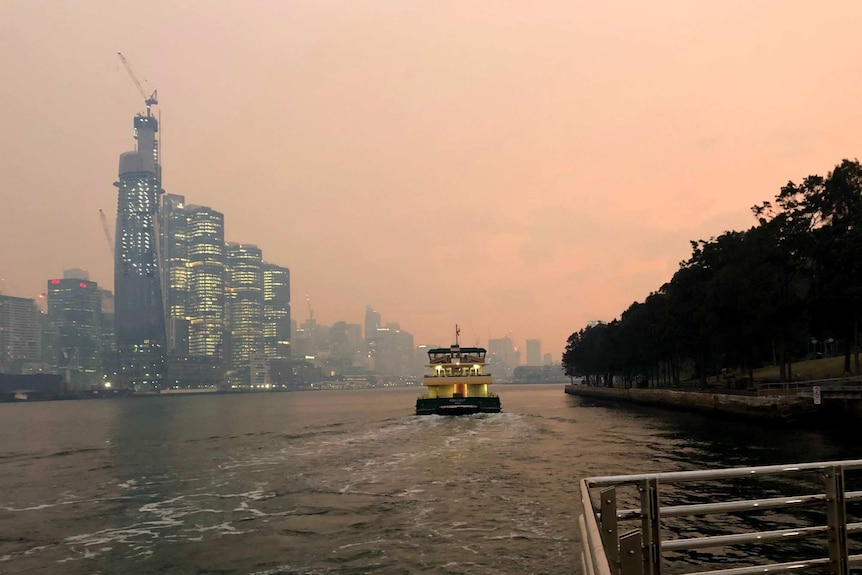 A ferry departs a wharf at Darling Harbour with Barrangaroo shrouded in smoke in the background.