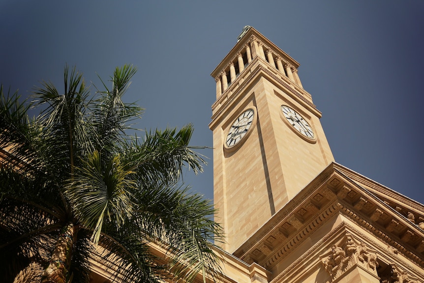 The clock tower at the Brisbane town hall, sandstone building, blue sky, palm tree.