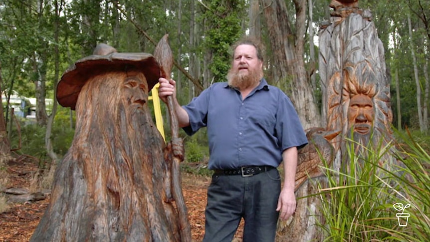 Man standing next to tree trunk carved into bearded man wearing a hat