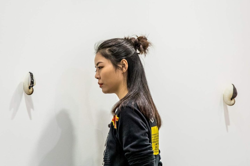 A young Asian woman is looking at a small art work in an exhibition.