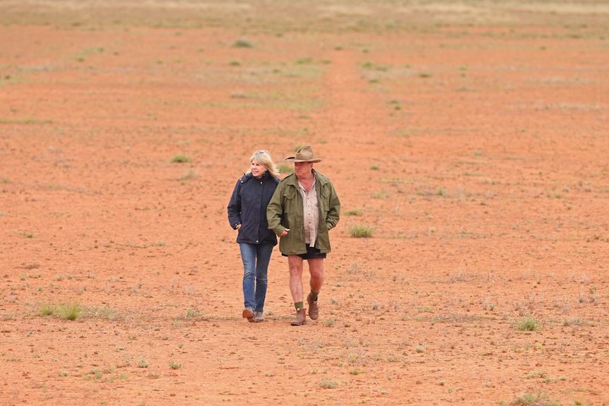 Sandy and Les Hiddins walk arm-in-arm over red dirt.
