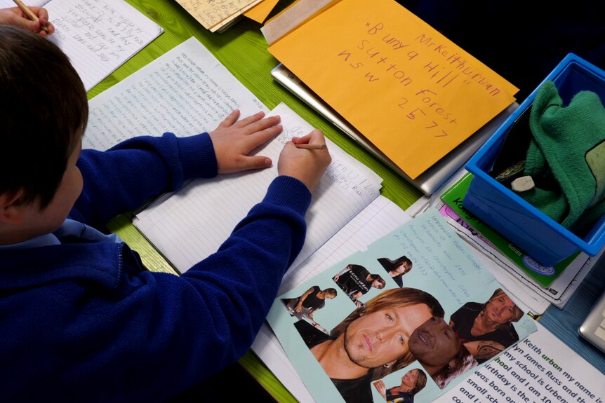 A student writing a letter with lots of cut out pictures of Keith Urban