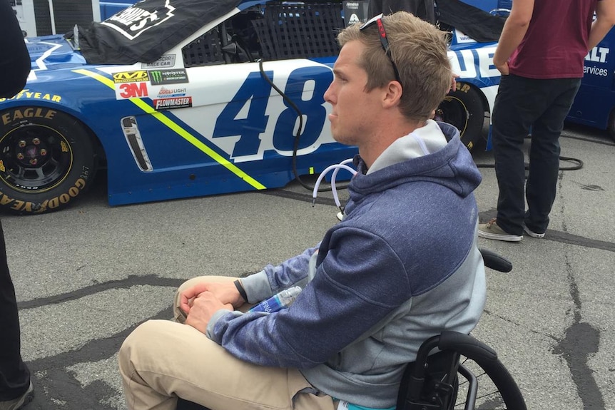 Sam Willoughby sits in his wheelchair next to a number 48 NASCAR