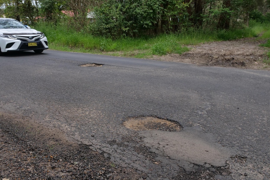 A car driving towards two potholes on a road