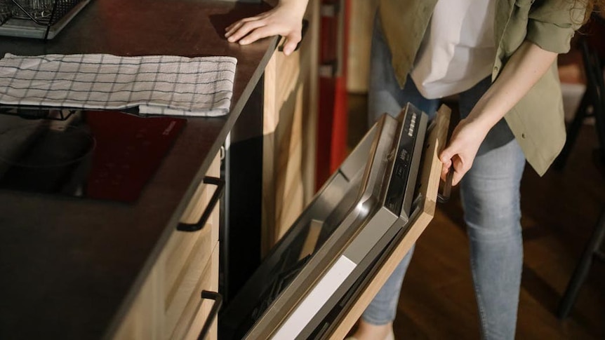 A woman opens a dishwasher.