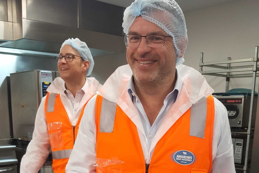 Two men in high visibility vests with plate of food in an industrial kitchen Andrews Meat Industries, Sydney