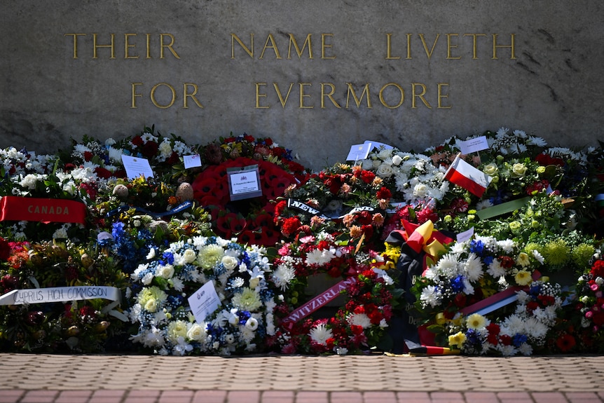A marble wall that reads "their name liveth for evermore" with floral wreaths laid at the bottom.