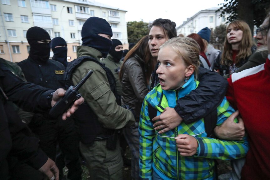 A woman shouts standing in front of a group of police wearing balaclavas during a rally in support of Maria Kolesnikova.
