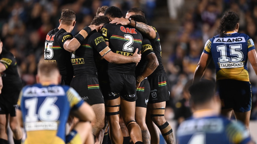 Panthers players celebrate with Eels players sitting blurred in the foreground