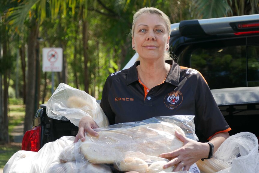 Blonde lady sits on the back of a ute with bags of bread in her lap
