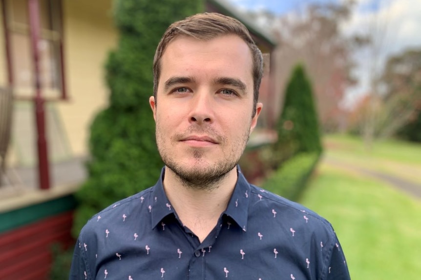 David Hill wears a navy blue shirt, stands in a garden and looks intently at the camera.