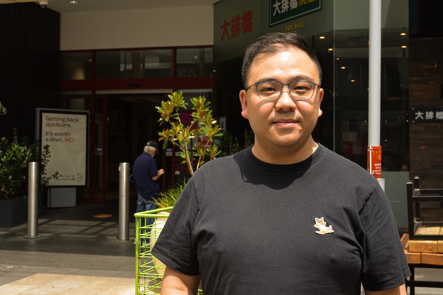 Richard Shi wearing a black top and glasses stands in front of a building