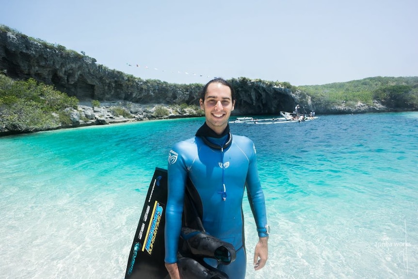 Adam Stern stands on a beach with his mono-fin