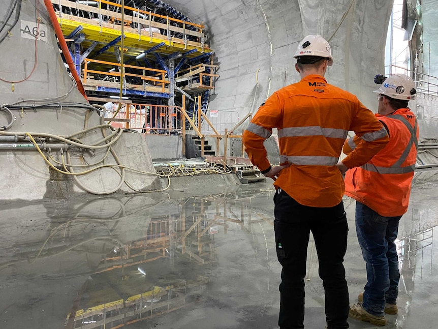 Two workers discuss the Martin Place metro rail station project, with tunnel in front of them.