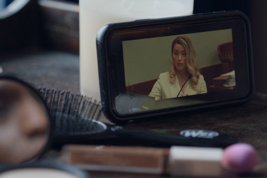 A video camera with Amber Heard in view wearing a yellow-coloured suit jacket and with hair free-flowing