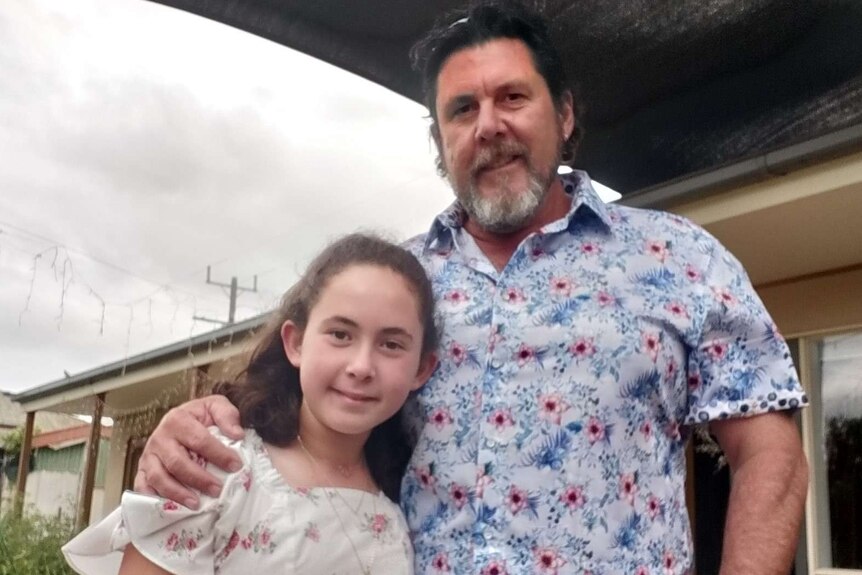 Father stands with arm around young daughter