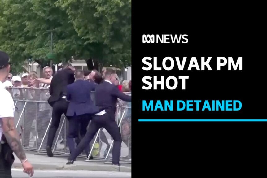 Slovak PM Shot, Man Detained: Men in suits react to something in a crowd. The crowd is separated by a metal barrier.