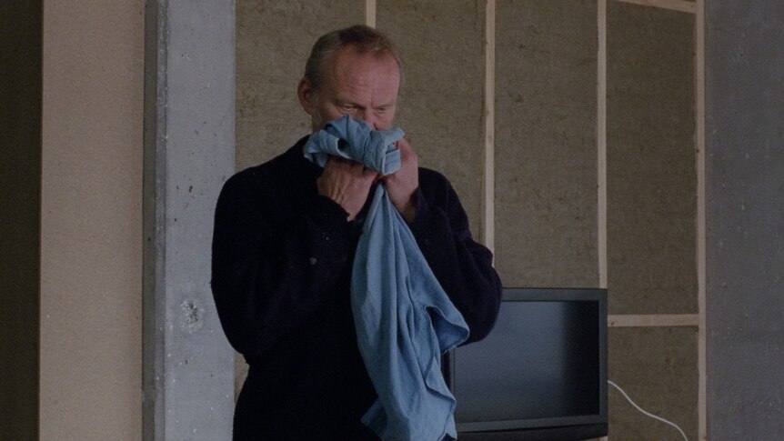 An older man sniffing an item of clothing from out of a box in the film A White, White Day