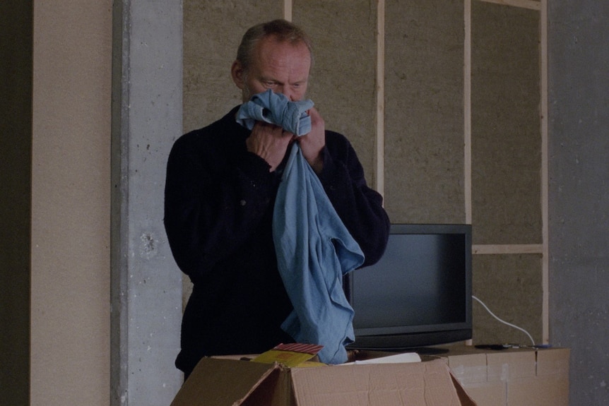 An older man sniffing an item of clothing from out of a box in the film A White, White Day