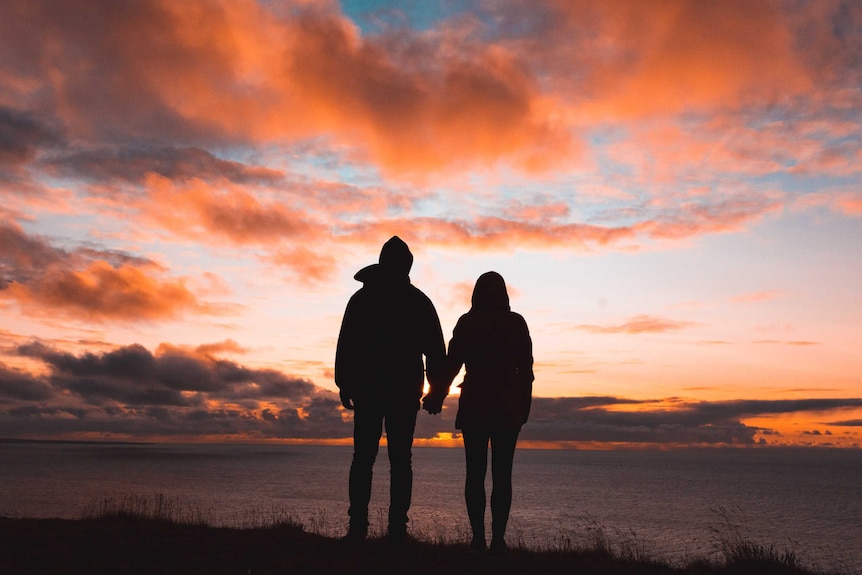 Two adults in silhouette looking at a sunset and holding hands