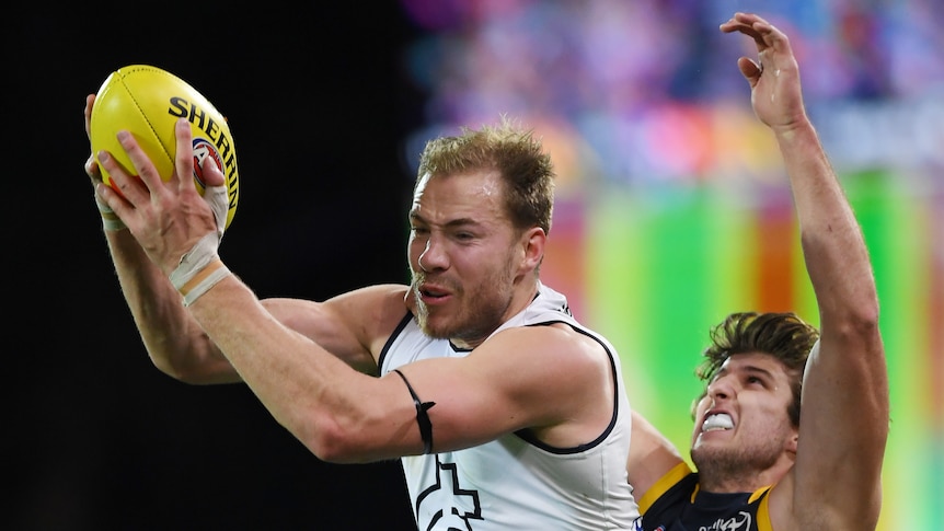 Carlton forward grabs the ball in two hands in front of him as an Adelaide defender grimaces behind him.